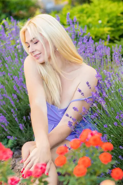 Leylak rengi bir elbisenin içinde uzun saçlı ve doğal makyajlı bir sarışının portresi lavanta çiçeklerinin arasında bir tarlada duruyor. Yaz sabahı