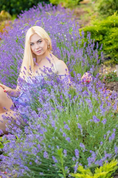 Leylak rengi bir elbisenin içinde uzun saçlı ve doğal makyajlı bir sarışının portresi lavanta çiçeklerinin arasında bir tarlada duruyor. Yaz sabahı
