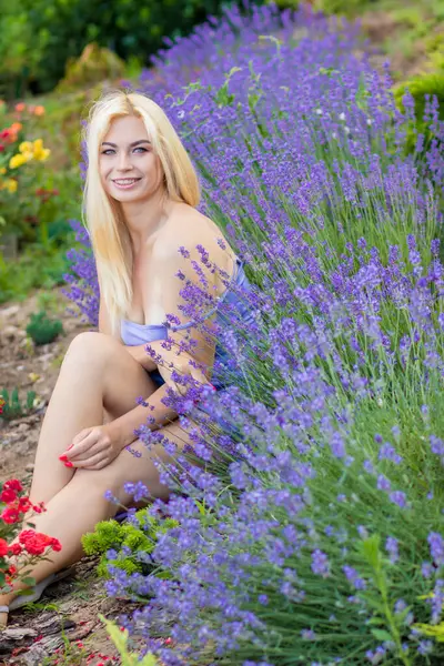 Leylak rengi bir elbisenin içinde uzun saçlı ve doğal makyajlı bir sarışının portresi lavanta çiçeklerinin arasında bir tarlada duruyor. Yaz sabahı