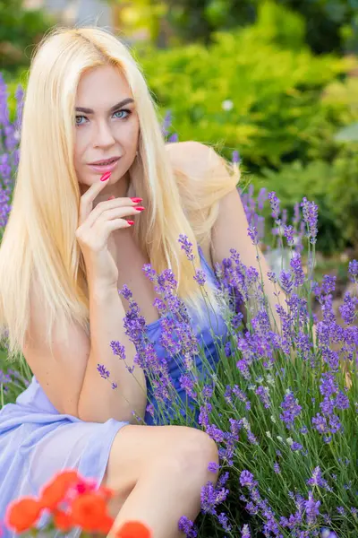 Leylak rengi bir elbisenin içinde uzun saçlı ve doğal makyajlı bir sarışının portresi lavanta çiçeklerinin arasında bir tarlada duruyor. Yaz sabahı