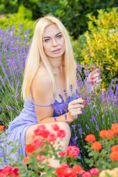 Leylak rengi bir elbisenin içinde uzun saçlı ve doğal makyajlı bir sarışının portresi lavanta çiçeklerinin arasında bir tarlada duruyor. Yaz sabahı