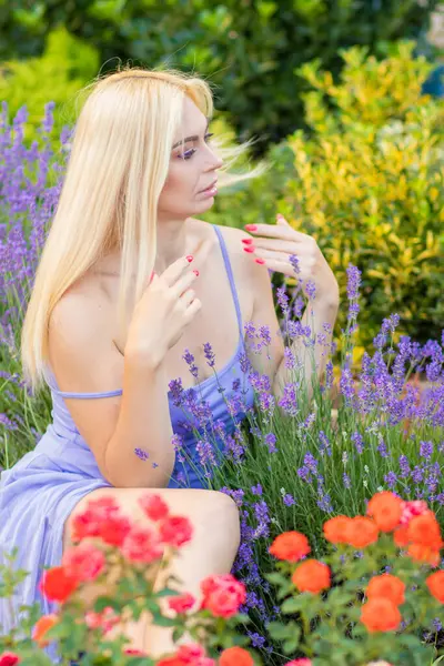 Leylak rengi bir elbisenin içinde uzun saçlı ve doğal makyajlı bir sarışının portresi lavanta çiçeklerinin arasında bir tarlada duruyor. Yaz sabahı