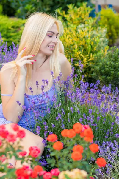 Leylak rengi bir elbisenin içinde uzun saçlı ve doğal makyajlı bir sarışının portresi lavanta çiçeklerinin arasında bir tarlada duruyor. Yaz sabahı