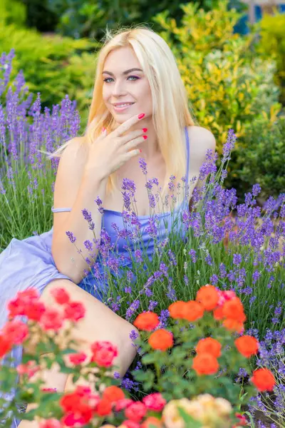 Leylak rengi bir elbisenin içinde uzun saçlı ve doğal makyajlı bir sarışının portresi lavanta çiçeklerinin arasında bir tarlada duruyor. Yaz sabahı