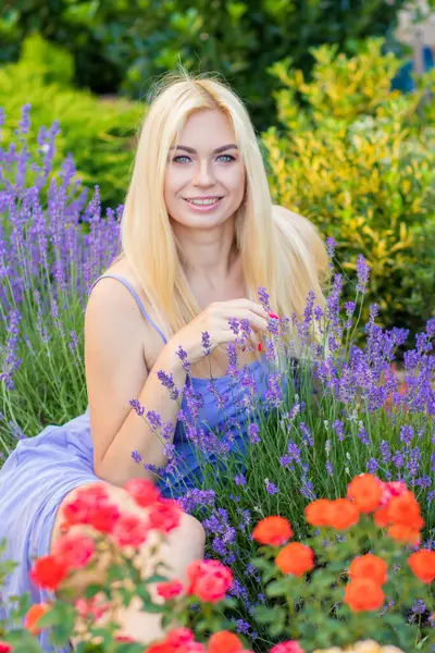 Leylak rengi bir elbisenin içinde uzun saçlı ve doğal makyajlı bir sarışının portresi lavanta çiçeklerinin arasında bir tarlada duruyor. Yaz sabahı