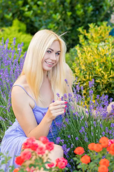 Leylak rengi bir elbisenin içinde uzun saçlı ve doğal makyajlı bir sarışının portresi lavanta çiçeklerinin arasında bir tarlada duruyor. Yaz sabahı