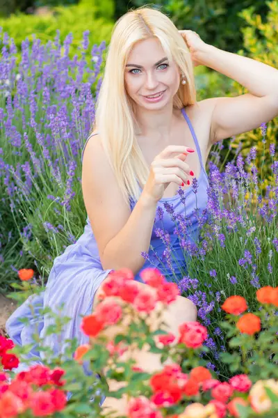 Leylak rengi bir elbisenin içinde uzun saçlı ve doğal makyajlı bir sarışının portresi lavanta çiçeklerinin arasında bir tarlada duruyor. Yaz sabahı