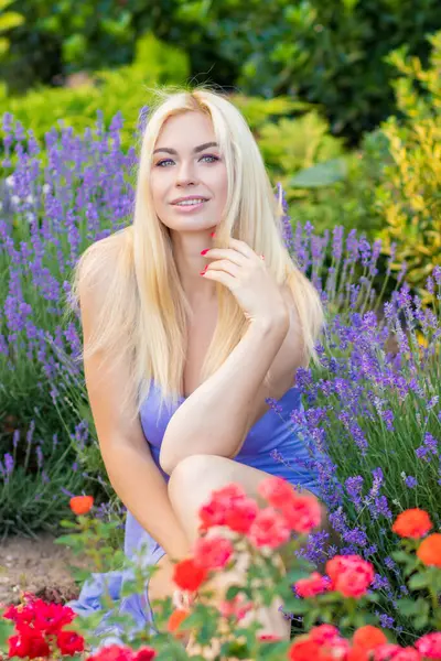 Leylak rengi bir elbisenin içinde uzun saçlı ve doğal makyajlı bir sarışının portresi lavanta çiçeklerinin arasında bir tarlada duruyor. Yaz sabahı