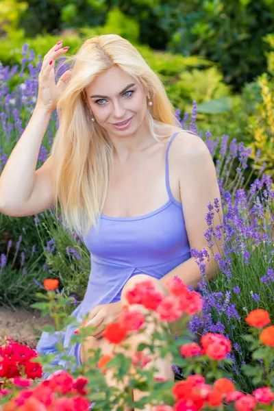 Leylak rengi bir elbisenin içinde uzun saçlı ve doğal makyajlı bir sarışının portresi lavanta çiçeklerinin arasında bir tarlada duruyor. Yaz sabahı