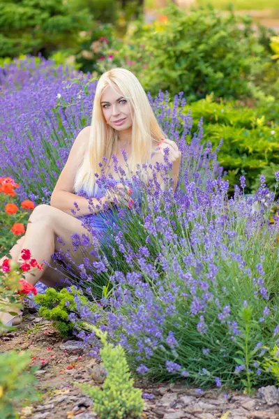 Leylak rengi bir elbisenin içinde uzun saçlı ve doğal makyajlı bir sarışının portresi lavanta çiçeklerinin arasında bir tarlada duruyor. Yaz sabahı
