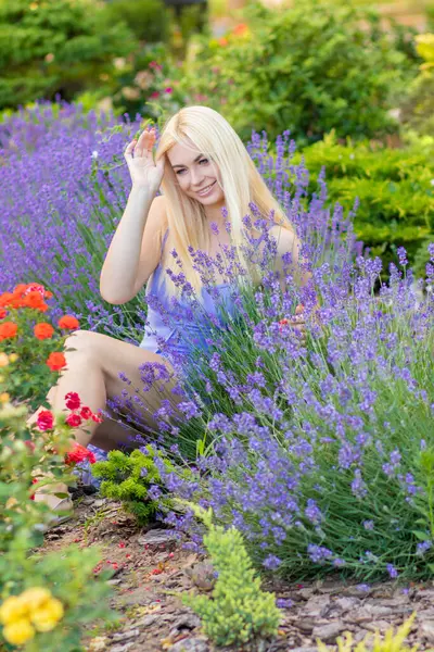 Leylak rengi bir elbisenin içinde uzun saçlı ve doğal makyajlı bir sarışının portresi lavanta çiçeklerinin arasında bir tarlada duruyor. Yaz sabahı