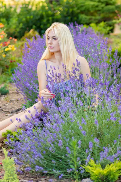 Leylak rengi bir elbisenin içinde uzun saçlı ve doğal makyajlı bir sarışının portresi lavanta çiçeklerinin arasında bir tarlada duruyor. Yaz sabahı