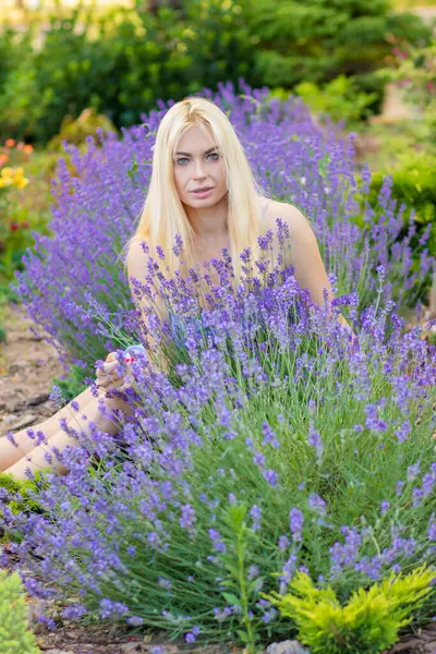 Leylak rengi bir elbisenin içinde uzun saçlı ve doğal makyajlı bir sarışının portresi lavanta çiçeklerinin arasında bir tarlada duruyor. Yaz sabahı