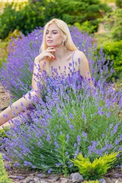 Leylak rengi bir elbisenin içinde uzun saçlı ve doğal makyajlı bir sarışının portresi lavanta çiçeklerinin arasında bir tarlada duruyor. Yaz sabahı