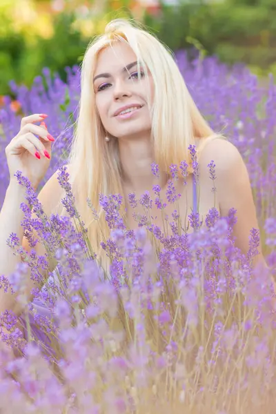 Leylak rengi bir elbisenin içinde uzun saçlı ve doğal makyajlı bir sarışının portresi lavanta çiçeklerinin arasında bir tarlada duruyor. Yaz sabahı