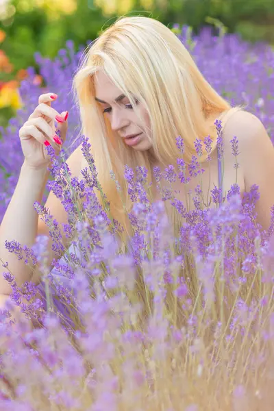 Leylak rengi bir elbisenin içinde uzun saçlı ve doğal makyajlı bir sarışının portresi lavanta çiçeklerinin arasında bir tarlada duruyor. Yaz sabahı