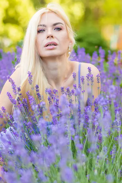 Leylak rengi bir elbisenin içinde uzun saçlı ve doğal makyajlı bir sarışının portresi lavanta çiçeklerinin arasında bir tarlada duruyor. Yaz sabahı