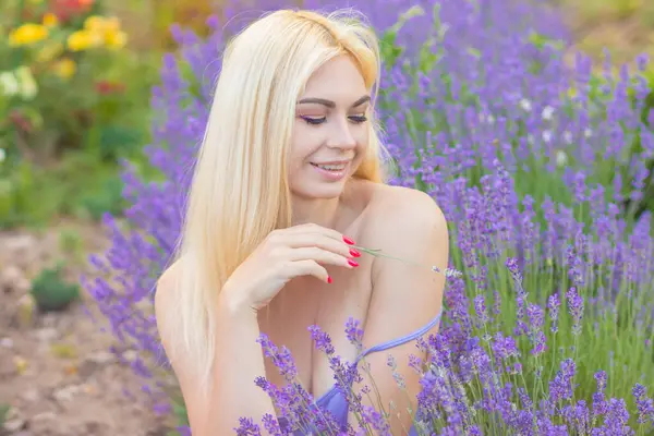 Leylak rengi bir elbisenin içinde uzun saçlı ve doğal makyajlı bir sarışının portresi lavanta çiçeklerinin arasında bir tarlada duruyor. Yaz sabahı