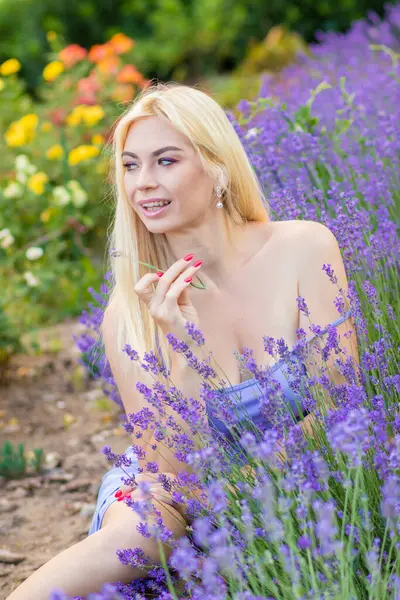 Leylak rengi bir elbisenin içinde uzun saçlı ve doğal makyajlı bir sarışının portresi lavanta çiçeklerinin arasında bir tarlada duruyor. Yaz sabahı