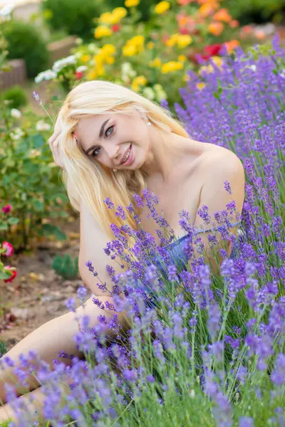 Leylak rengi bir elbisenin içinde uzun saçlı ve doğal makyajlı bir sarışının portresi lavanta çiçeklerinin arasında bir tarlada duruyor. Yaz sabahı