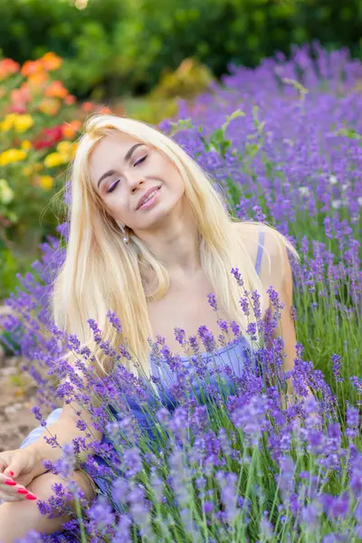 Leylak rengi bir elbisenin içinde uzun saçlı ve doğal makyajlı bir sarışının portresi lavanta çiçeklerinin arasında bir tarlada duruyor. Yaz sabahı