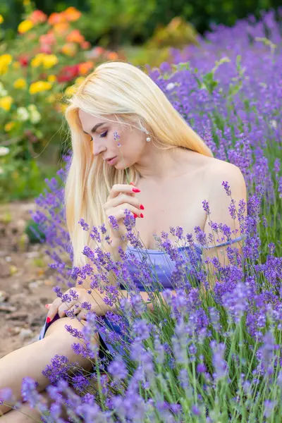 Leylak rengi bir elbisenin içinde uzun saçlı ve doğal makyajlı bir sarışının portresi lavanta çiçeklerinin arasında bir tarlada duruyor. Yaz sabahı
