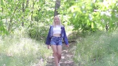 Sarışın kadın yaz günü parkta yürüyor.