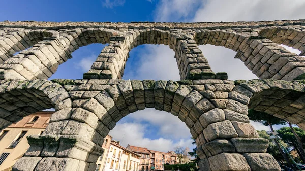 view of the roman aqueduct of Segovia with the houses through the eyes of the aqueduct and the blue sky