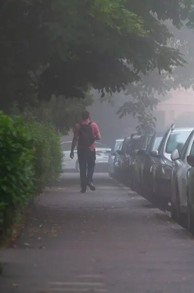Unrecognizable man walking on the street. Fog in the early morning. View from behind. Real people.