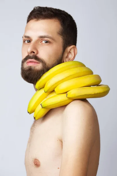 ビーガンライフスタイルのコンセプト 肩に熟した黄色のバナナを持つハンサムな若い男の肖像画は 灰色の背景に隔離された頬に触れる スタジオショット — ストック写真