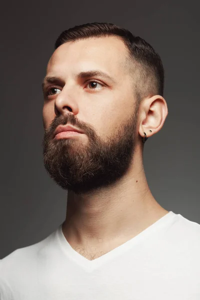 Male beauty concept. Portrait of proud charismatic active 30-year-old man posing over dark gray background. Perfect haircut. Hipster style. Close up. Studio shot