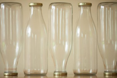 Süt için birkaç boş cam şişe açık bej arka plan üzerinde ahşap masanın üzerinde duruyor. Bazılarının dibi kalkık. Gün ışığı. Avantgarde tarzı. Kapalı çekim