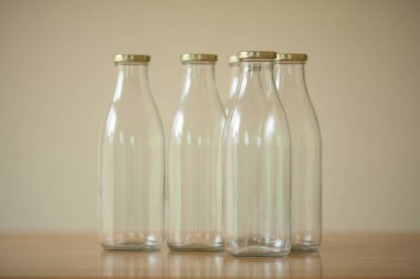 Süt için birkaç boş cam şişe açık bej arka planda, ahşap masada duruyor. Gün ışığı. Kapalı çekim