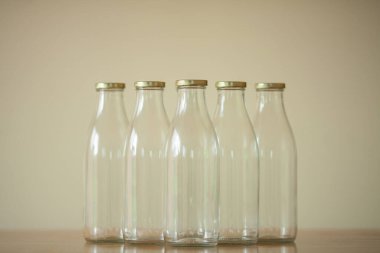 Süt için birkaç boş cam şişe açık bej arka planda, ahşap masanın üzerinde duruyor. Gün ışığı. Metin uzayı. Kapalı çekim