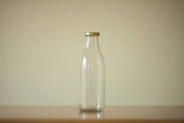 軽いベージュの背景の上の木のテーブルの上に立っているミルクのための1つの空のガラスびん コピースペース インドアショット — ストック写真