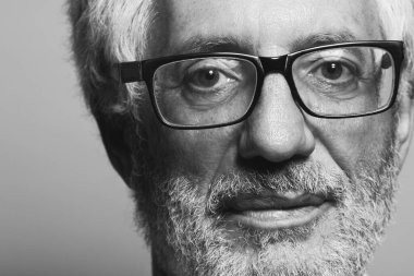 Göz giyimi konsepti. Gri arka planda poz veren 60 yaşındaki bir adamın portresi. Kapatın. Kopyalama uzayı. Blcak ve White stüdyo çekimi