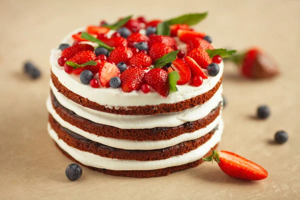 Bakery, candy shop concept. Close-up image of amazing chocolate and butter cream cake decorated with different fresh berries. Natural light. Indoor shot