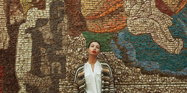 Think big, be creative concept. Portrait of young fashion model in trendy street style clothing posing over wall with abstract mosaic. Text space. Outdoor shot