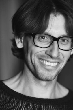 Erkek güzellik konsepti. Siyah örgü süveter giyen gülen yakışıklı adamın duygusal portresi. Parlak uzun saçlar, parlak mükemmel bir gülümseme. Kapatın. Moda göz giysisi. Siyah-beyaz kapalı çekim