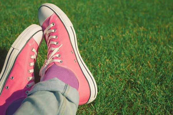 Hand knotted laces pink sneakers on nature. Men's legs in blue jeans, lavender socks on green grass. Copy-space. Outdoor shot