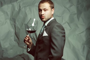 Sommelier concept. Emotive portrait of handsome stylish man in elegant classic dark gray suit drinking red wine. Baroque retro style. Studio shot