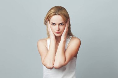 Close-up portrait of a young woman in white sleeveless shirt imitating hear no evil concept on gray background. Human emotions, expressions, communication. Text space. Studio shot clipart