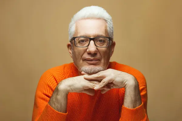 在任何年龄都是不可思议的 眼镜的概念 穿着橙色毛衣的60岁时髦男子的画像 米黄色 白色背景 漂亮的发型 光滑的灰白头发 手握锁腕 复制空间 图库图片