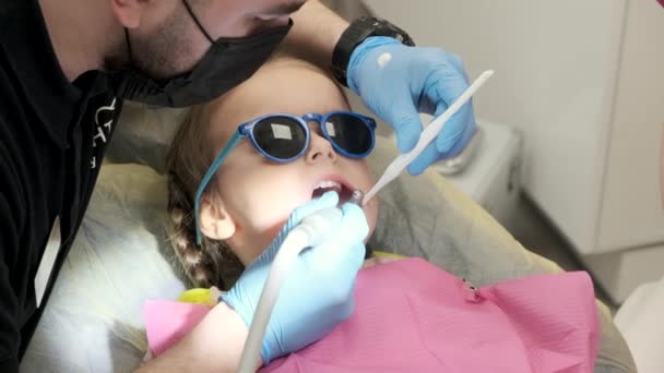 かわいい子供の女の子は歯医者と治療中の歯科アームチェアに横たわっています — ストック動画
