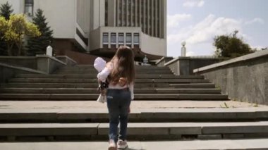 Beyaz tişörtlü ve kot pantolonlu kız merdivenlerden yukarı çıkıyor..