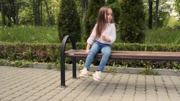 白いシャツの4歳のかわいい女の子はベンチで公園でマシュマロを食べる — ストック動画