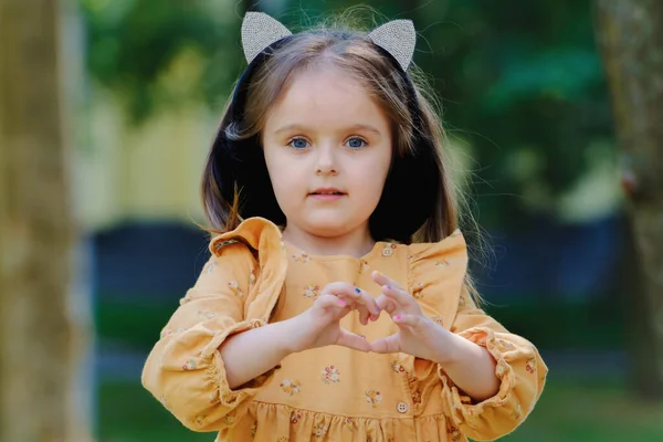 公園でかわいい女の子の肖像画と彼女の手で心のサインを示しています — ストック写真