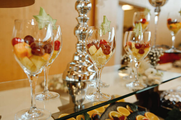 A lot of wine glasses with fresh fruit on the table at the ceremony. Selective focus.