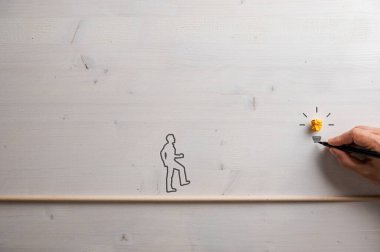 Tahta bir yaya köprüsünden geçerek erkek eline doğru yürüyen bir adamın silüeti kavramsal bir görüntü ve fikir görüntüsüyle bir ampul çiziyor..