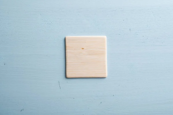 パステルブルーの木製の背景に配置されたシンプルな無地の空白の木製のタイル — ストック写真